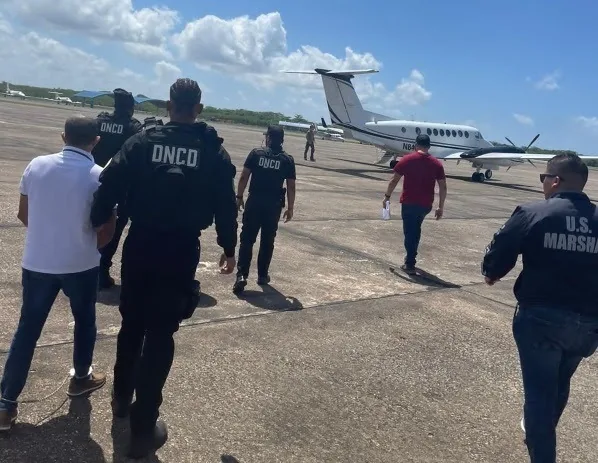 Agentes de la DNCD y un alguacil de Estados Unidos escoltan a detenidos hacia una aeronave durante un operativo de extradición en una pista dominicana (foto de archivo)